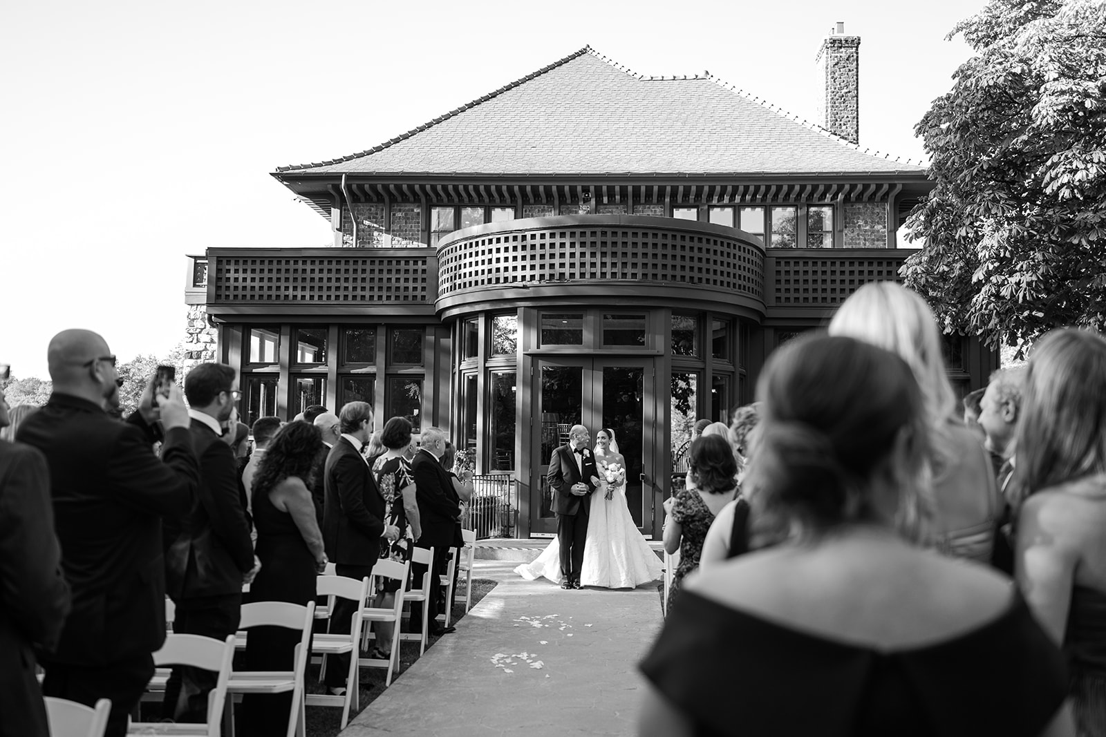 Black and white film photo of the bride and her father walking out of the mansion to start the ceremony.